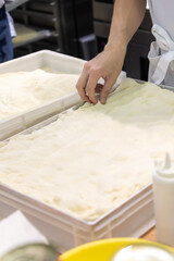 Close-up side view of male cook hands preparing thin rectangular pizza dough on professional kitchen table in pizzeria or italian restaurant. Soft focus. Copy space. Food service business theme.