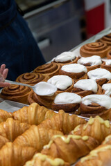 Close-up side view of baker putting whipped cream on top of fresh baked brown cinnamon buns using spoon on professional kitchen table. Soft focus. Food preparation and decoration theme.