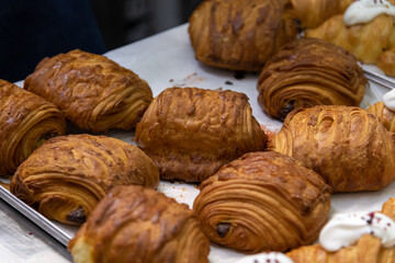 Close-up side view of fresh baked brown croissants with chocolate cream lying on baking tray on professional kitchen table. Soft focus. Copy space. Puff pastry theme.