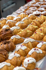Close-up side view of various fresh baked puff pastry items (croissants with different fillings with edible flowers and cinnamon rolls) on baking tray on professional kitchen table. Food background.