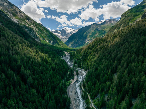 Aerial view of lush green valley with a serene river and majestic mountains, Gran Paradiso National Park, Cogne, Italy.