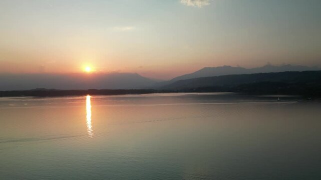 Aerial view of serene sunset over Lago di Viverone with majestic mountains and calm water, Viverone, Italy.