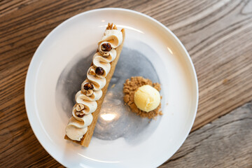Napoleon cake with vanilla ice cream and cookie crumbs on the side in an organic high-end coffee shop, delicately plated dessert on a wooden table, rich nutty flavor, hazelnut flavor