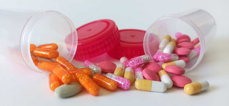 Pill capsules spill out of two plastic containers across a clean white surface to represent pharmaceutical distribution and healthcare management.
