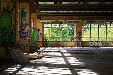 Graffiti-covered walls illuminated by sunlight in an abandoned space with broken windows and decay