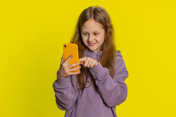 Young preteen child girl kid using mobile smartphone typing new post on web, sms message, watching video, browsing, addiction of social media networks. Teenager children isolated on yellow background
