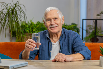 Thirsty senior man hold glass of natural filtered aqua drinking still water preventing dehydration....