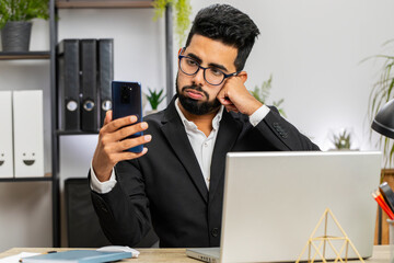 Indian businessman freelancer use smartphone typing browsing, loses becoming surprised sudden...