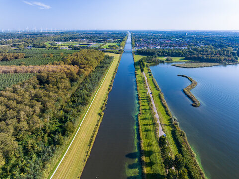 Aerial view of canal Hoge Vaart between forest Vaartsluisbos and lake Noorderplassen with wind turbines and scenic greenery, Almere, Netherlands.