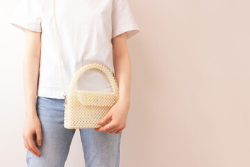 Woman with a handmade bag made from pearl imitation beads over her shoulder in front of beige background.
