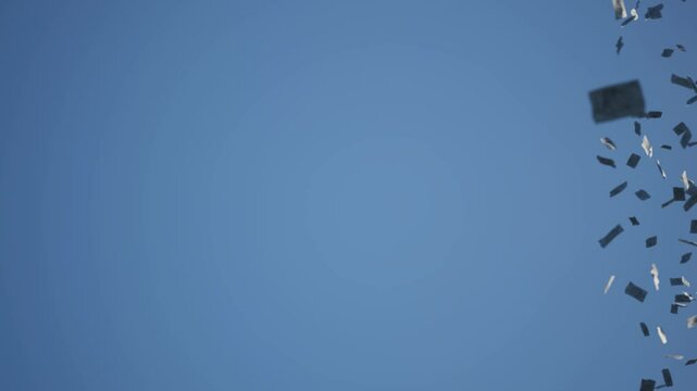 Papers fly across the sky. The wind blows the money notes through the air.