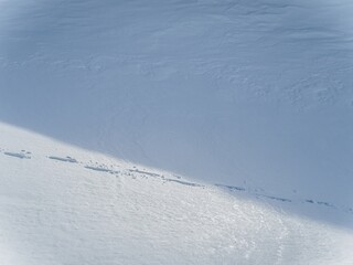 Snowy mountain slope with footprints and shadows