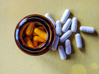 Top view of pills capsules in pill bottle on yellow background. White pills capsules medicine or ...