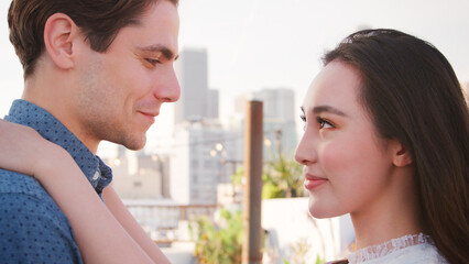 Portrait Of Romantic Couple Looking At Each Other On Rooftop Terrace With City Skyline In Background