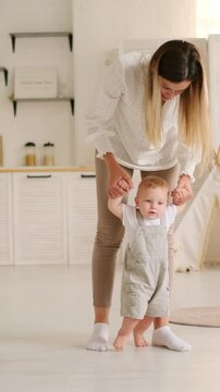 mom teaches the baby to walk at home, the baby boy learns to walk by taking the first steps holding his mother's hand