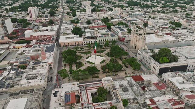 Aerial view of vibrant Merida Plaza with historic architecture, greenery, and a Mexican flag, Merida, Mexico.