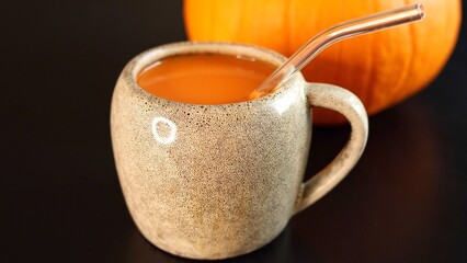 Pumpkin beverage inside ceramic mug, glass straw, pumpkin placed behind, vibrant autumn harvest setup showcasing fresh seasonal produce, organic textures, warm rustic tones, cozy atmosphere.