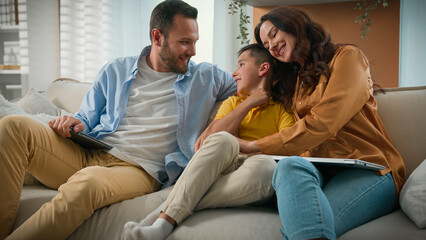 Happy Caucasian family mom dad son parents child kid boy tickling having fun relax on sofa together...