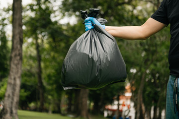 Hand holding garbage black bag putting in to trash to clean. Clearing, pollution, and plastic concept..