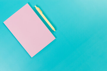 Top view of pink notebook, yellow pen on blue background. School, office wallpaper. Flat lay, copy space.