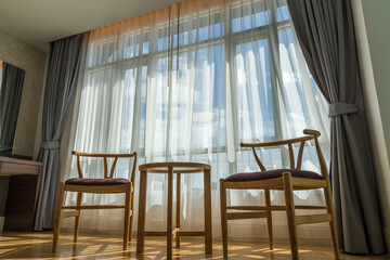 The luxurious room has wooden chairs and a background of white curtains with a view of the sky.Interior of a hotel room with chairs and curtains. Nobody inside