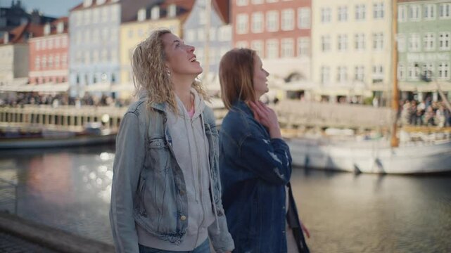 Two Tourists Strolling Along Nyhavn Canal With Colorful Buildings