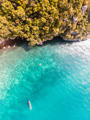 Aerial view of a serene coastline with a small boat on turquoise waters.