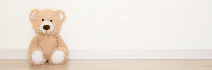 Smiling brown soft teddy bear sitting on wooden floor at light gray wall background. Empty place for text, quote or sayings. Closeup. Wide banner. Front view.