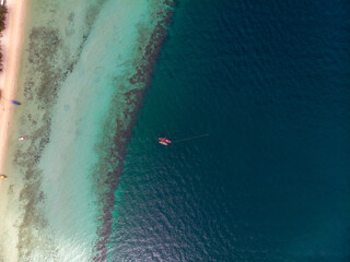 Aerial view of a serene coastline with a small boat on clear blue waters.