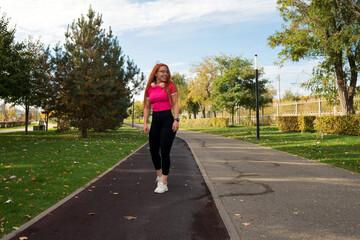 Woman walking in park, wearing headphones and sportswear