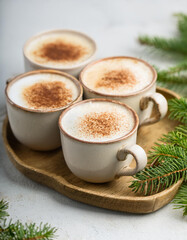 Ceramic mugs of cappuccino with foam on wooden tray. Tasty drink. Hot beverage. Green fir branches