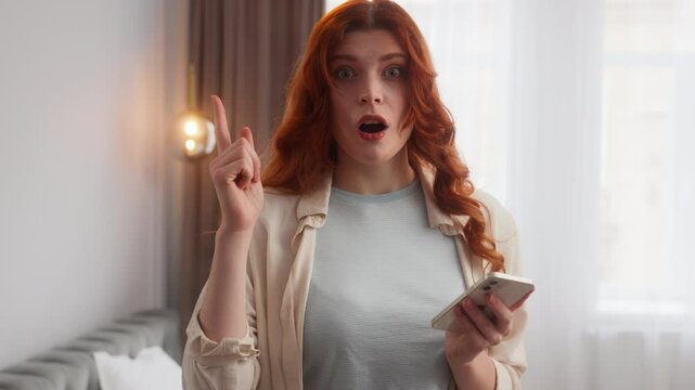 Pensive Caucasian woman typing mobile phone chatting texting in Internet app. Excited girl raise index finger open mouth eureka emotion at home smart inspired female generate idea solution find answer