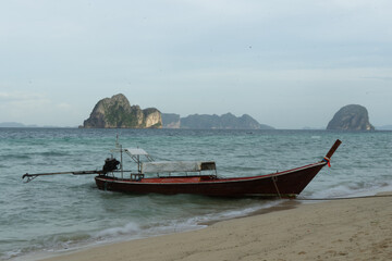 Fototapeta premium A solitary boat rests on a tranquil beach with distant islands in the background.