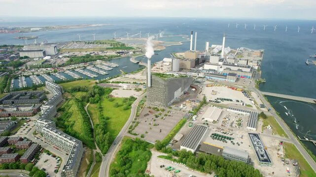 Aerial view of copenhill power plant with wind turbines and boats in the harbour, copenhagen, denmark.