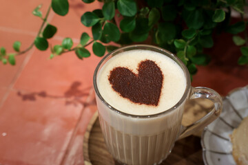 Une tasse de capuccino en verre  avec un cœur en poudre de chocolat. 