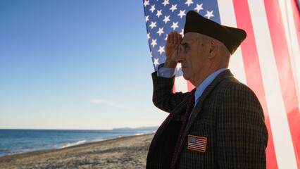 War Veteran Salutes Looking At The Ocean Near The American Flag