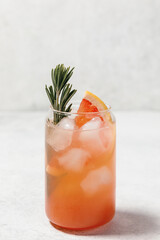 Grapefruit cocktail with rosemary garnish in a glass served on white table. Vibrant, refreshing drink perfect for summer menu or cocktail recipes. Greyhound, lemonade, paloma, mocktail.