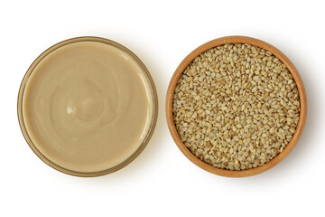 Tahini sauce in glass jar and sesame seeds in wooden bowl on white background