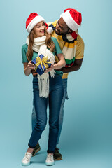 A happy couple celebrates with a gift, wearing festive hats and scarves in a cozy winter atmosphere.