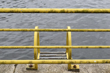 Fototapeta premium Rusted Yellow Steel Ladder and Handrail Beside Calm Waters of River 