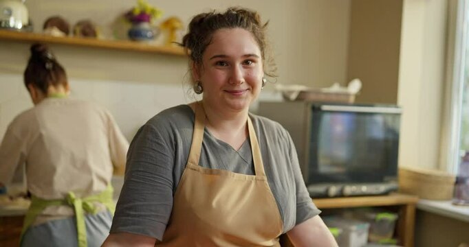Portrait of a happy girl with curly hair as a baker in a beige apron who stands at a table in a bakery while working