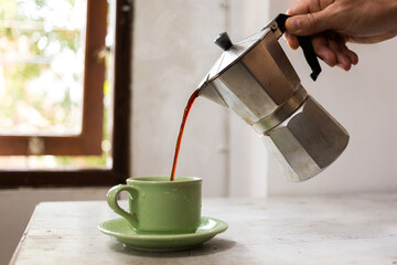 A hand pours hot, strong coffee from the coffee maker. Delicious invigorating morning coffee at home.