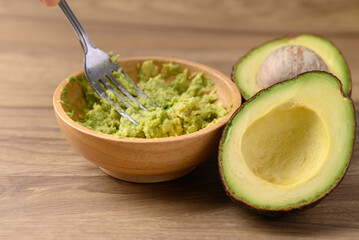 Smashing avocado in wooden bowl by fork