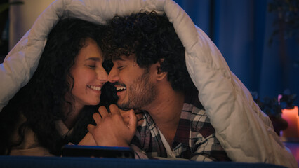 Multiracial couple man and woman at night home win mobile phone bet good news achievement triumph excited with online winning victory smartphone high five at evening couch under blanket gadget addict