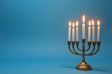 Menorah with lit candles on blue background for Hanukkah celebration with copy space