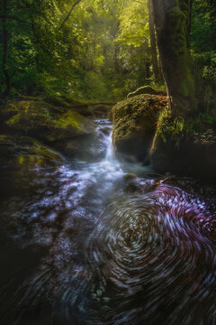 View of serene Silver River waterfall surrounded by lush trees and mossy rocks, Huelgoat, France.