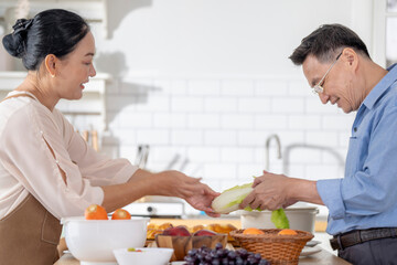 A woman prepares fresh vegetables in a cozy kitchen, while a man assists in the background. The scene emphasizes a warm and healthy lifestyle with a focus on fresh produce and home cooking.