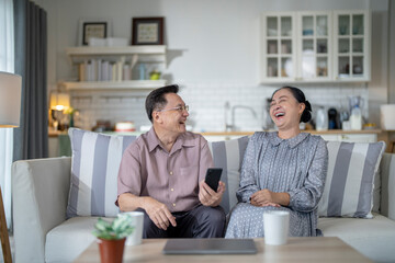 An elderly couple sits together in their cozy living room, smiling and enjoying a moment as they look at something on a smartphone. Their warmth and affection capture a peaceful home atmosphere.