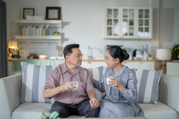 Fototapeta premium An elderly couple enjoys a peaceful moment at home, sharing smiles and drinks. The warm and cozy atmosphere emphasizes their deep connection, happiness, and the comfort of spending time together.