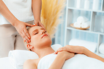 Fototapeta premium Caucasian woman enjoying relaxing anti-stress head massage and pampering facial beauty skin recreation leisure in dayspa modern light ambient at luxury resort or hotel spa salon. Quiescent